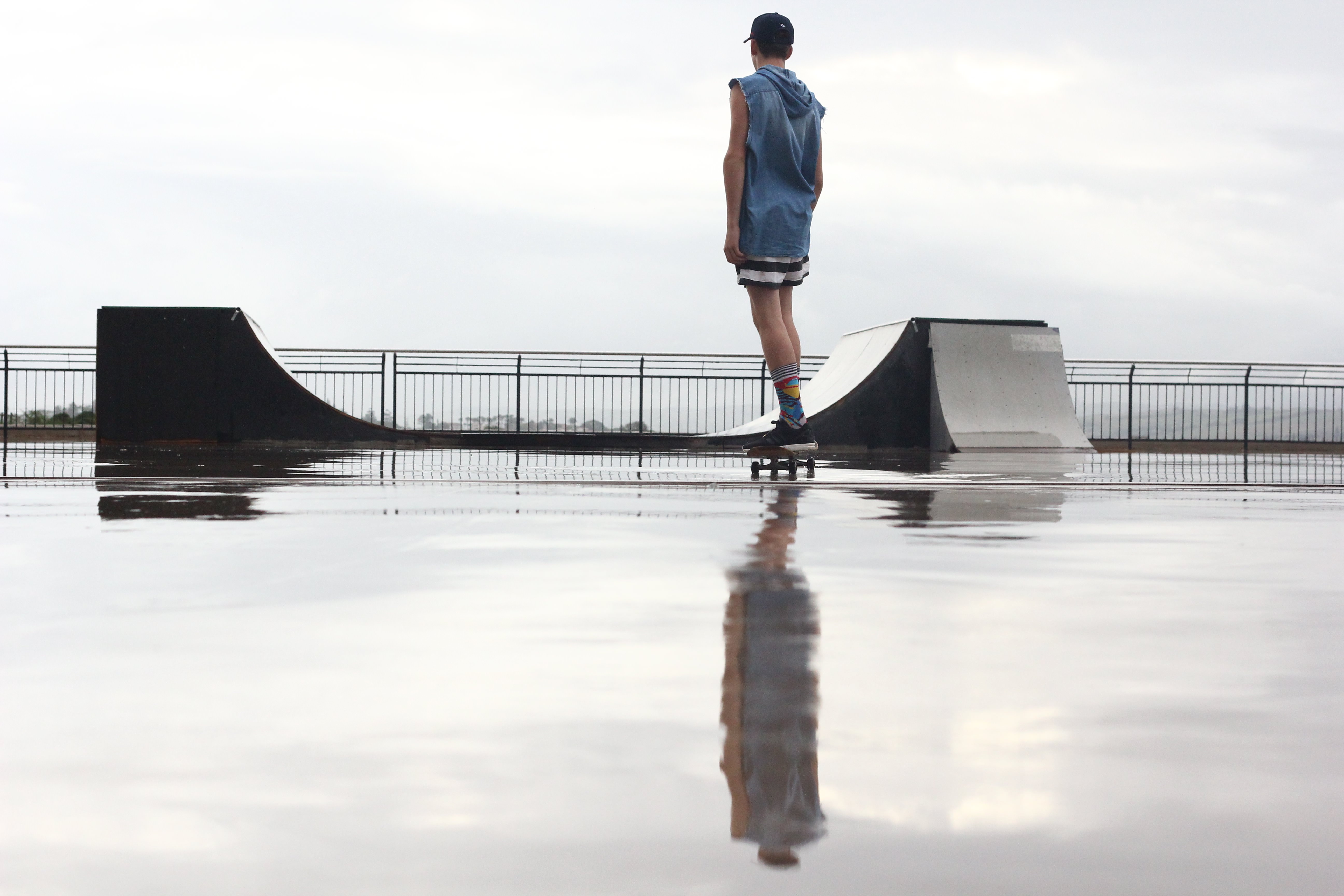 Boy standing adjacent to skateboard ramp, wet pavement, looking into distance