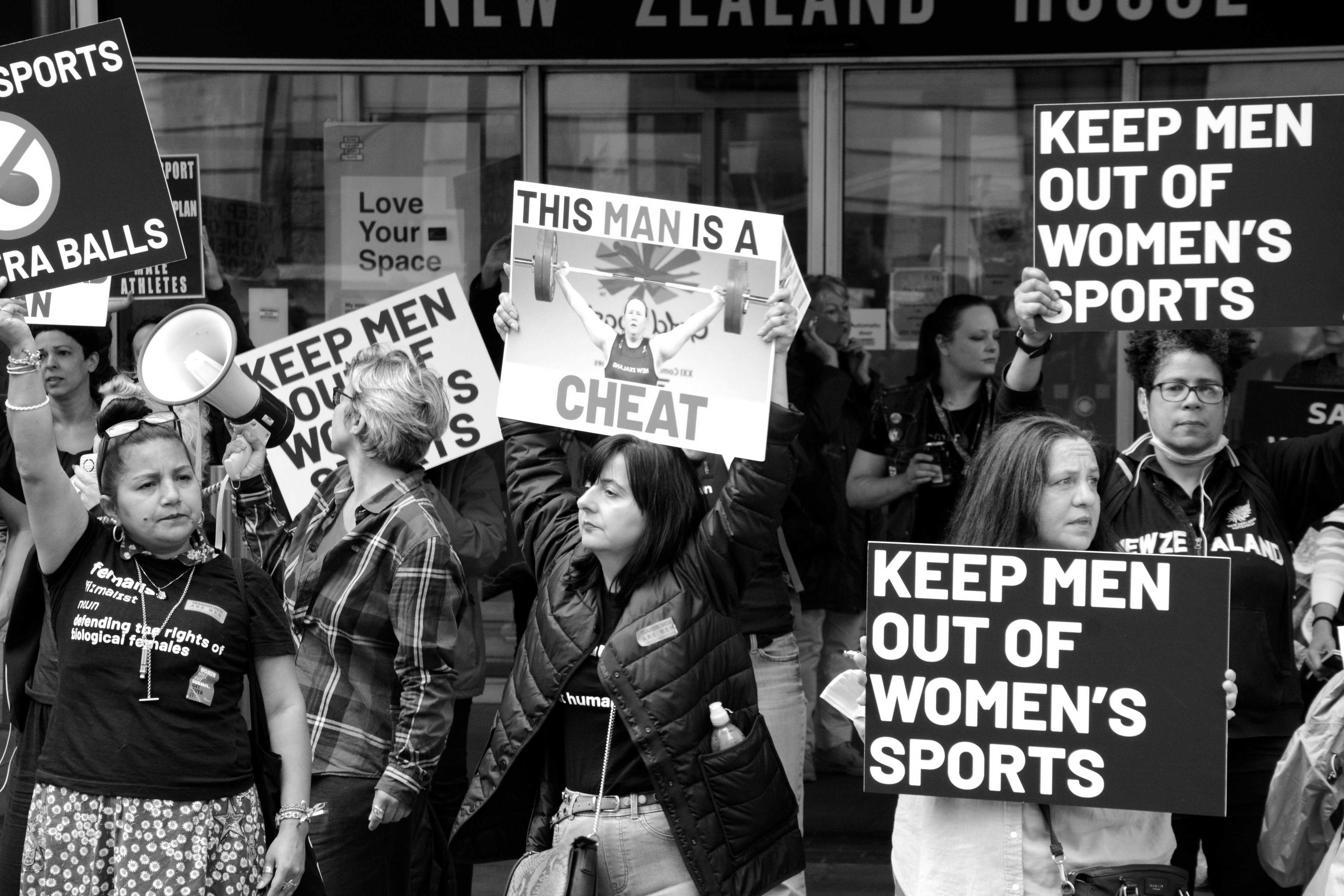 Demonstrators holding plackards saying keep (transgender) men out of women's sport