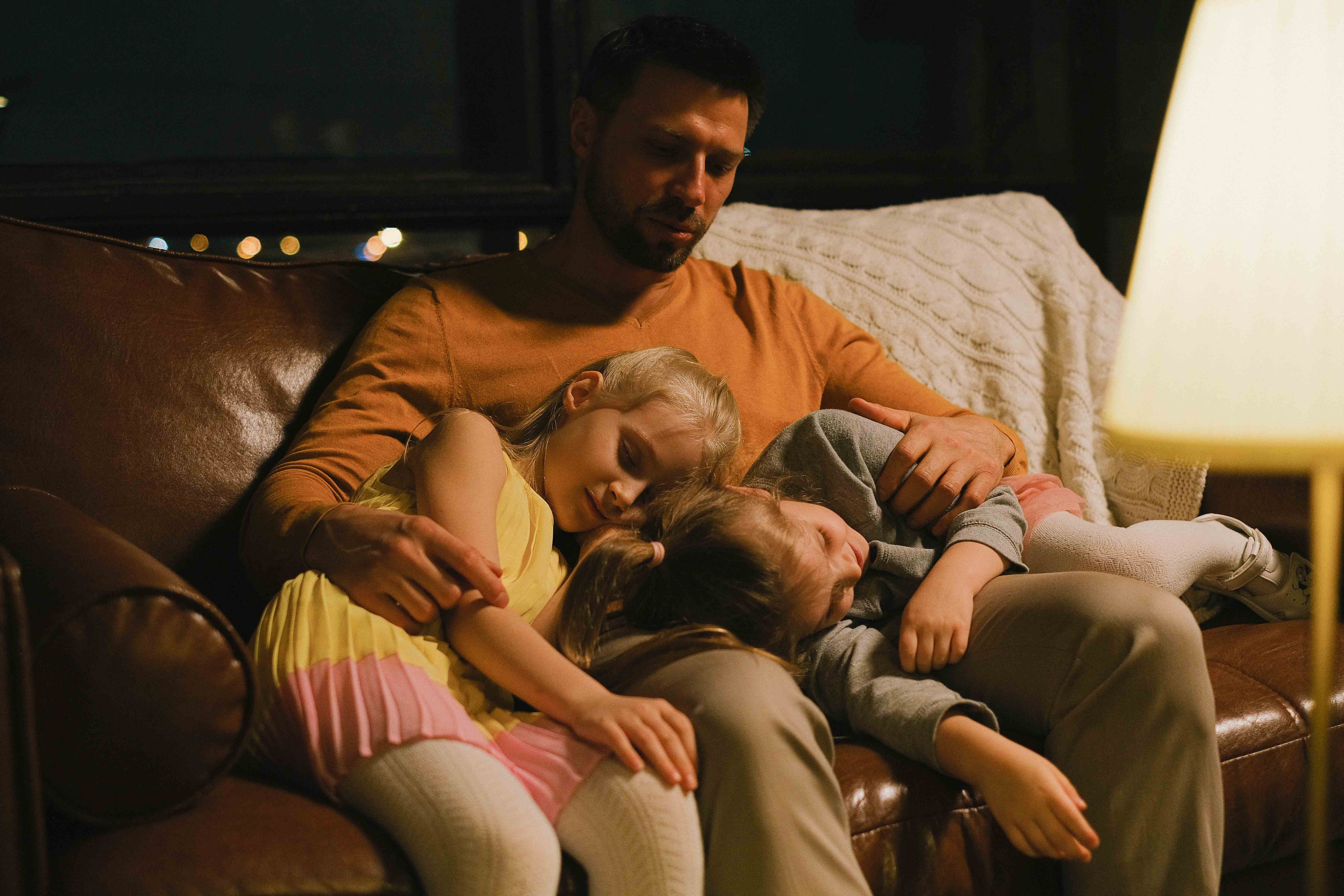 Father sitting on couch with two kids, asleep on his lap
