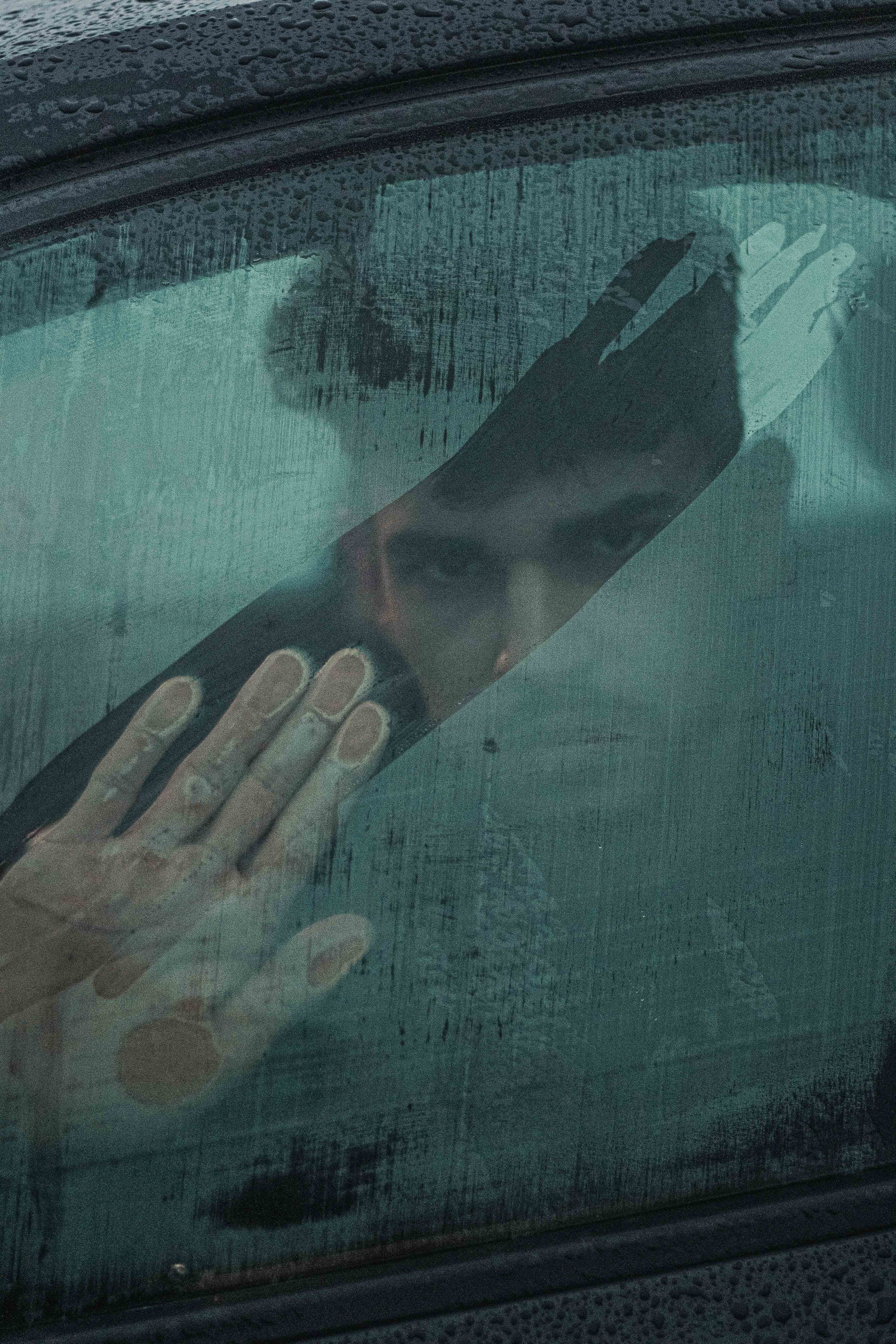 Man looking from inside car through a foggy window, and has smeared fog with hand leaving stripen car with side windo