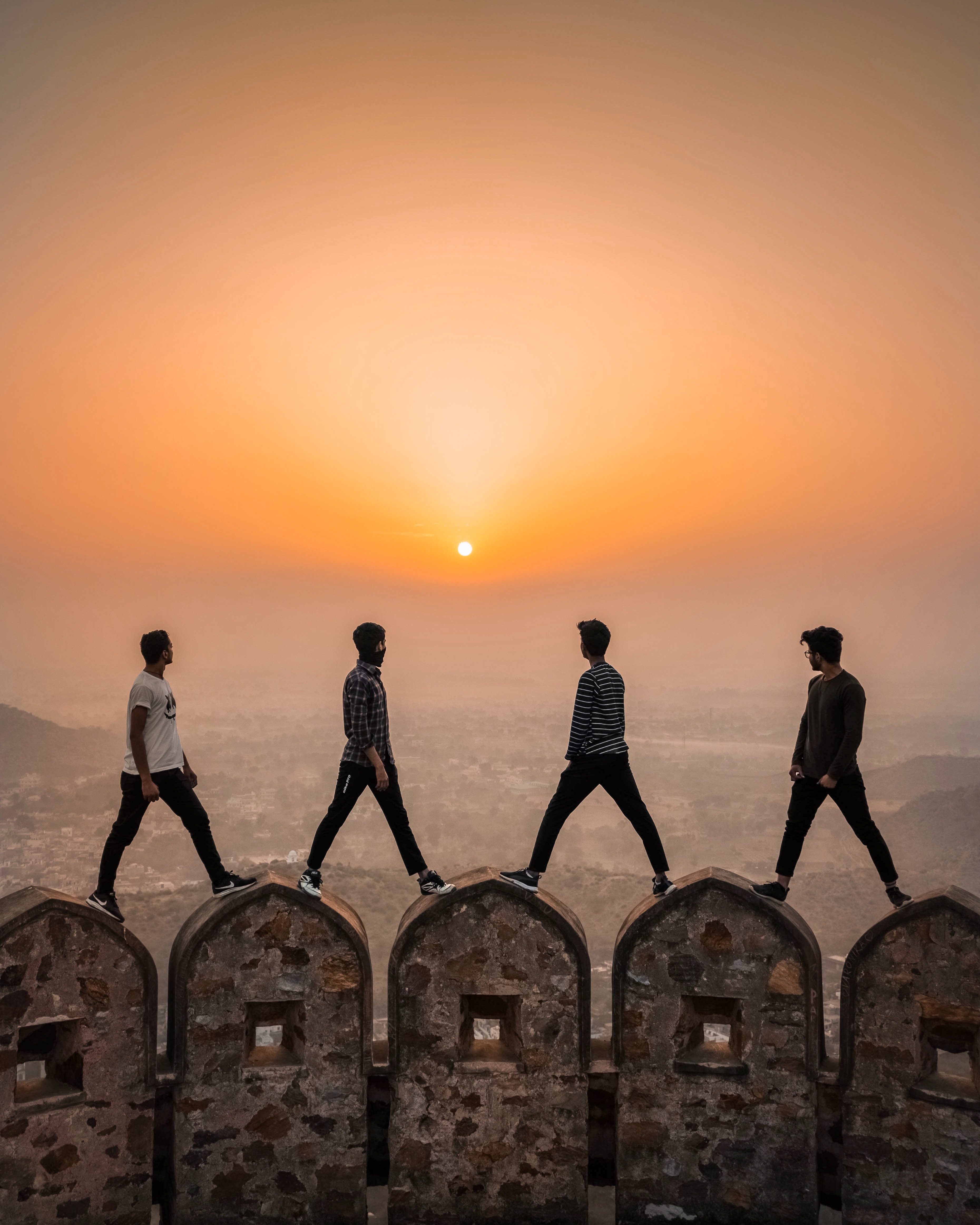 Four men, each standing on a turret, overlooking valley , looking at sunset, orange sky
